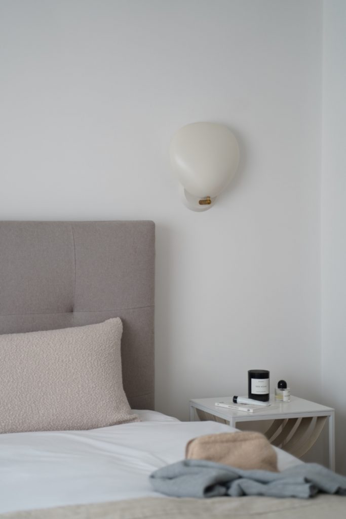 Nordic style bedroom with white sheets and Gubi wall lamp